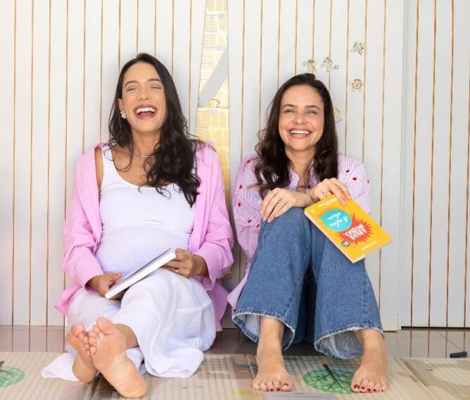 Iza e Izadora, fundadoras do noMami, sentadas no chão sorrindo